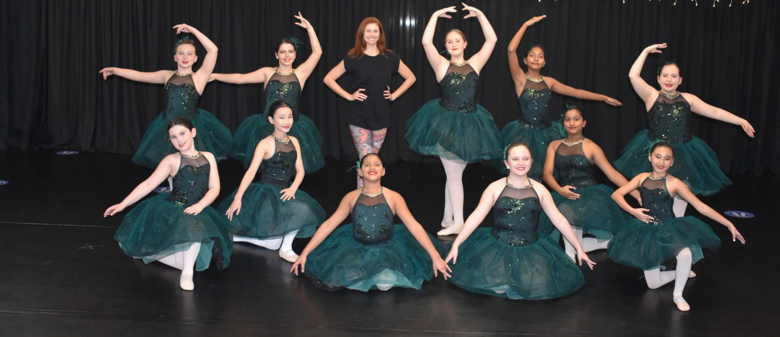 A ballet group in emerald tutus with one of our teachers, arms in fifth.