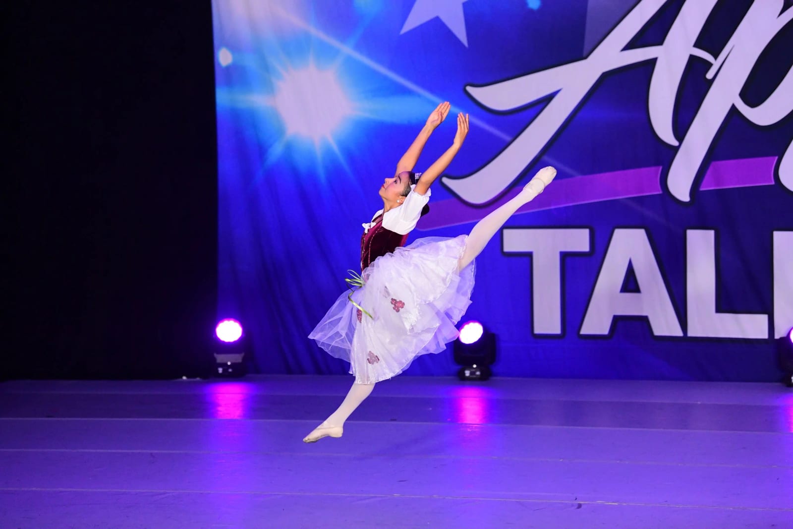 One of our ballet dancers in arabesque on a competition stage under purple light.
