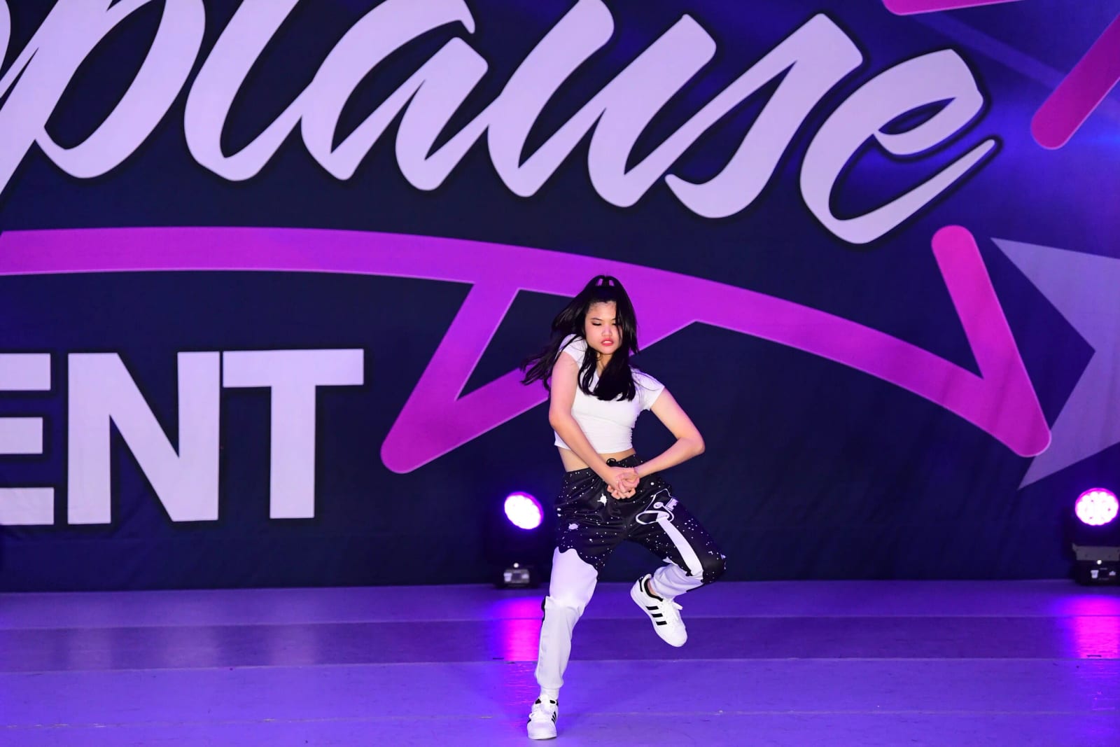A hip-hop soloist in white in front of a purple Applause Talent competition backdrop.