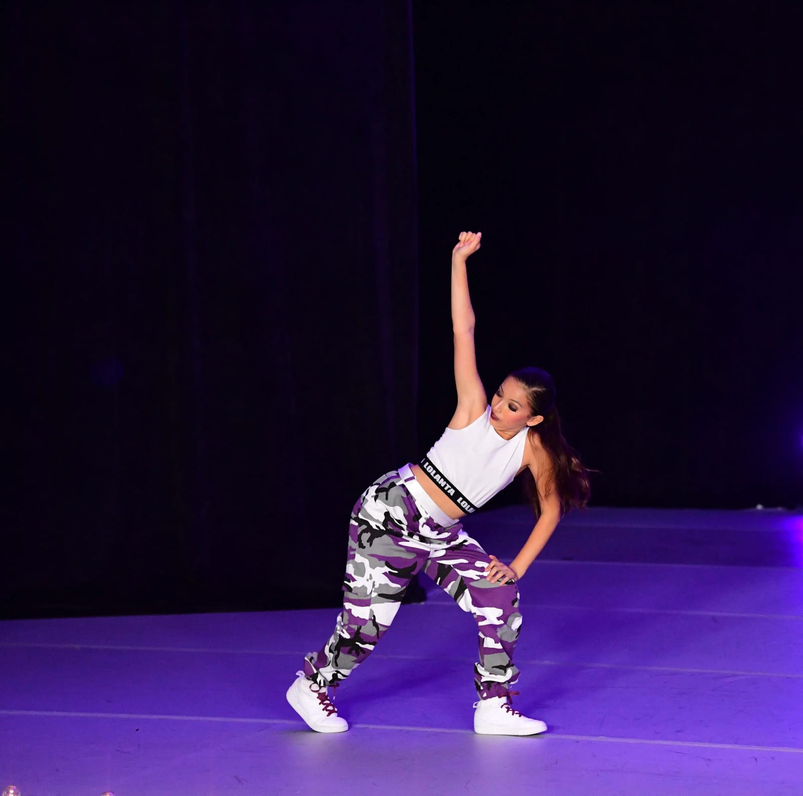 A hip-hop soloist in camo pants under purple stage light.