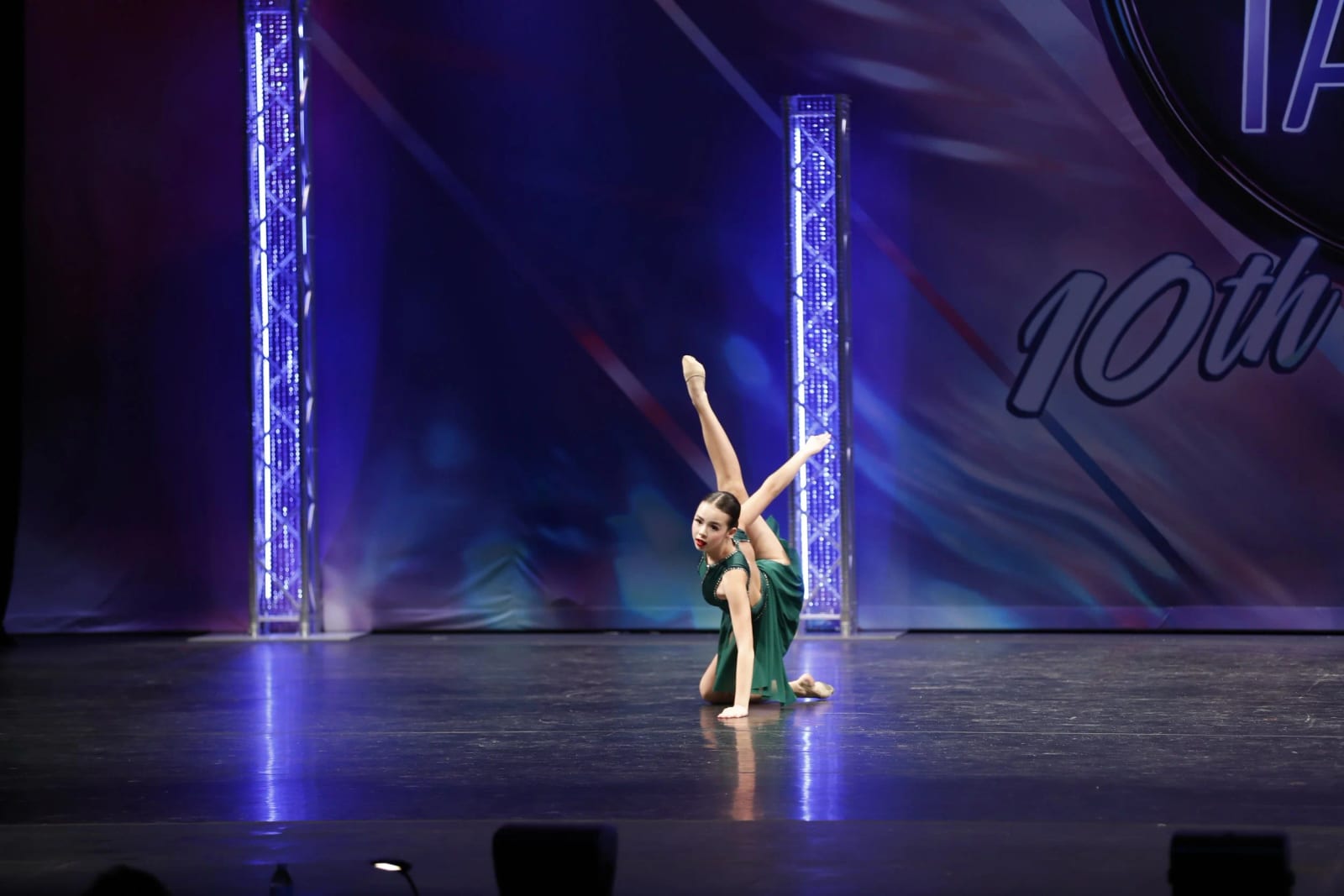 A solo dancer holding an extension on a competition stage between two lighting towers.